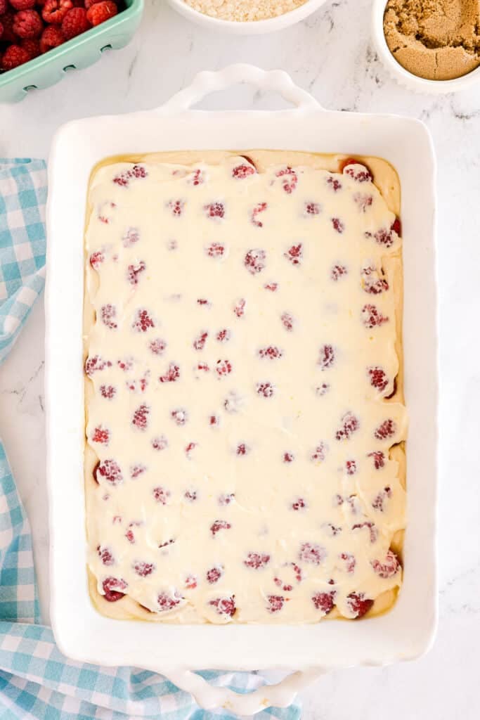 White baking dish filled with raw raspberry cream cheese coffee cake batter, raspberries visible throughout.