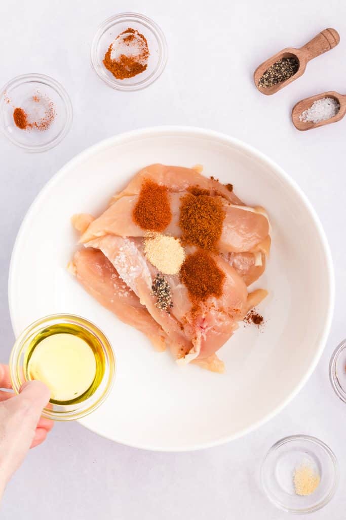 raw chicken tenders topped with seasonings in a bowl.