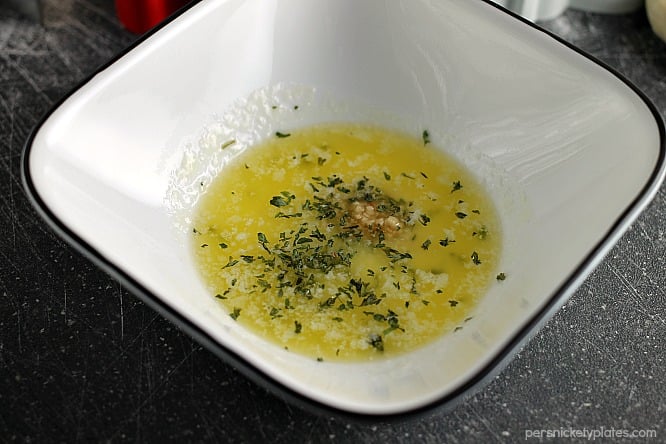 butter garlic herb mixture in a white bowl to brush onto dinner rolls