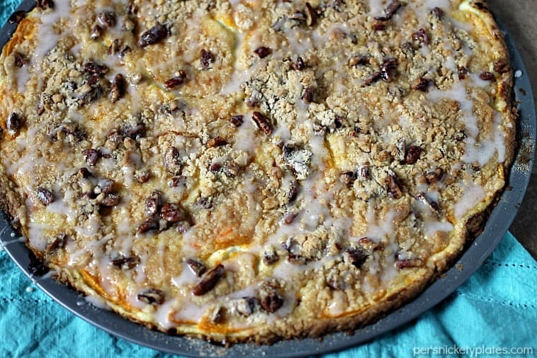 Peach Crumble Fruit Pizza is made on a cake batter crust, piled with thinly sliced fresh peaches and topped with a crumble and pecans and drizzled with a cinnamon sugar glaze. | www.persnicketyplates.com