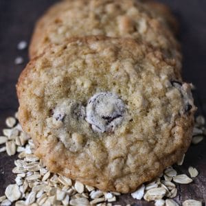 three ranger cookies on a dark wood table and spilled oats