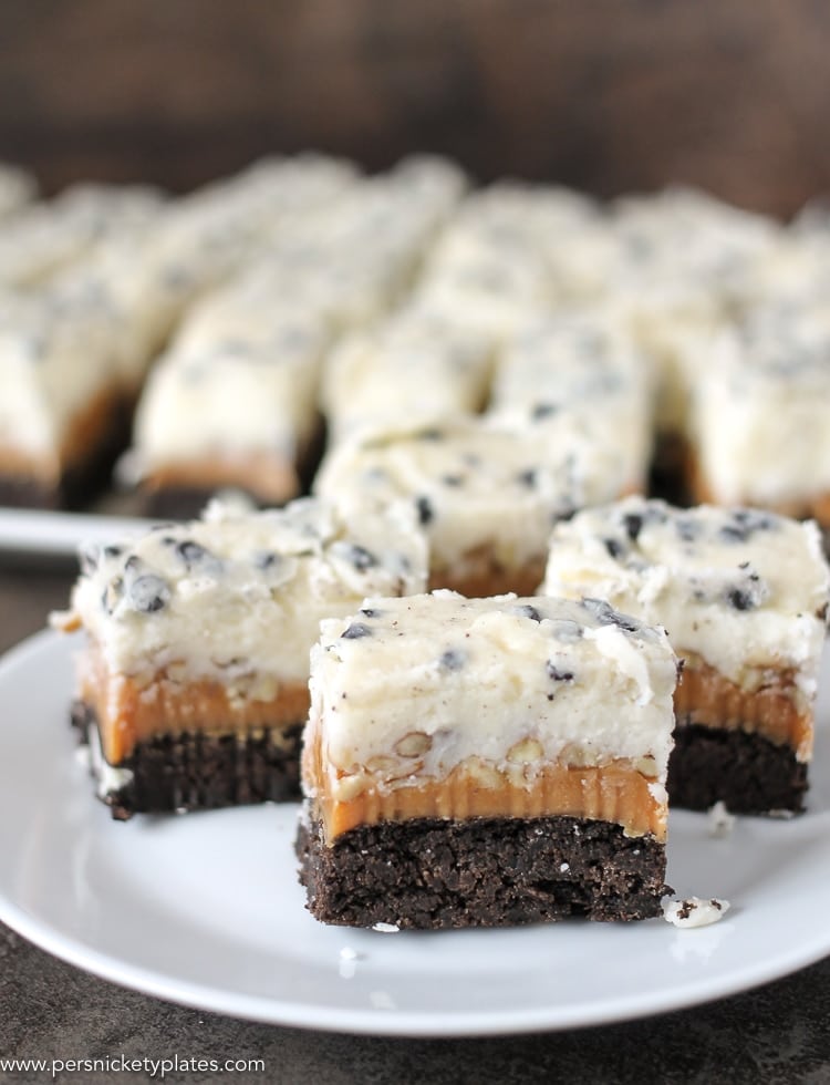Cookies and Cream Caramel Layer Bars start with a layer of Pillsbury Cookies 'n Creme cookie dough, topped with a layer of caramel, chopped pecans, frosting, then finished with melted Cookies 'n Creme candy bars. I hope your sweet tooth is ready! three cookies and cream caramel layer bars on a plate