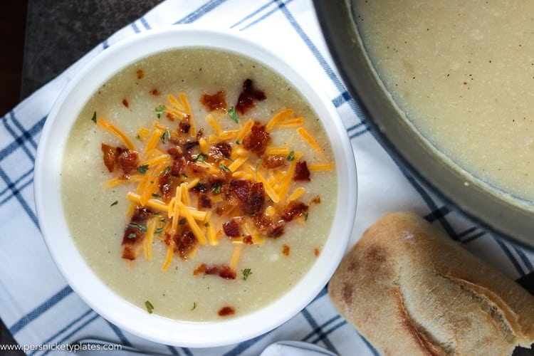 Loaded Potato and Cauliflower Soup has everything you love about loaded potato soup - it's creamy, full of smoky bacon, and cheese - but is lightened up with the use of cauliflower! | www.persnicketyplates.com bowl of loaded potato soup with pot of soup and chunk of bread
