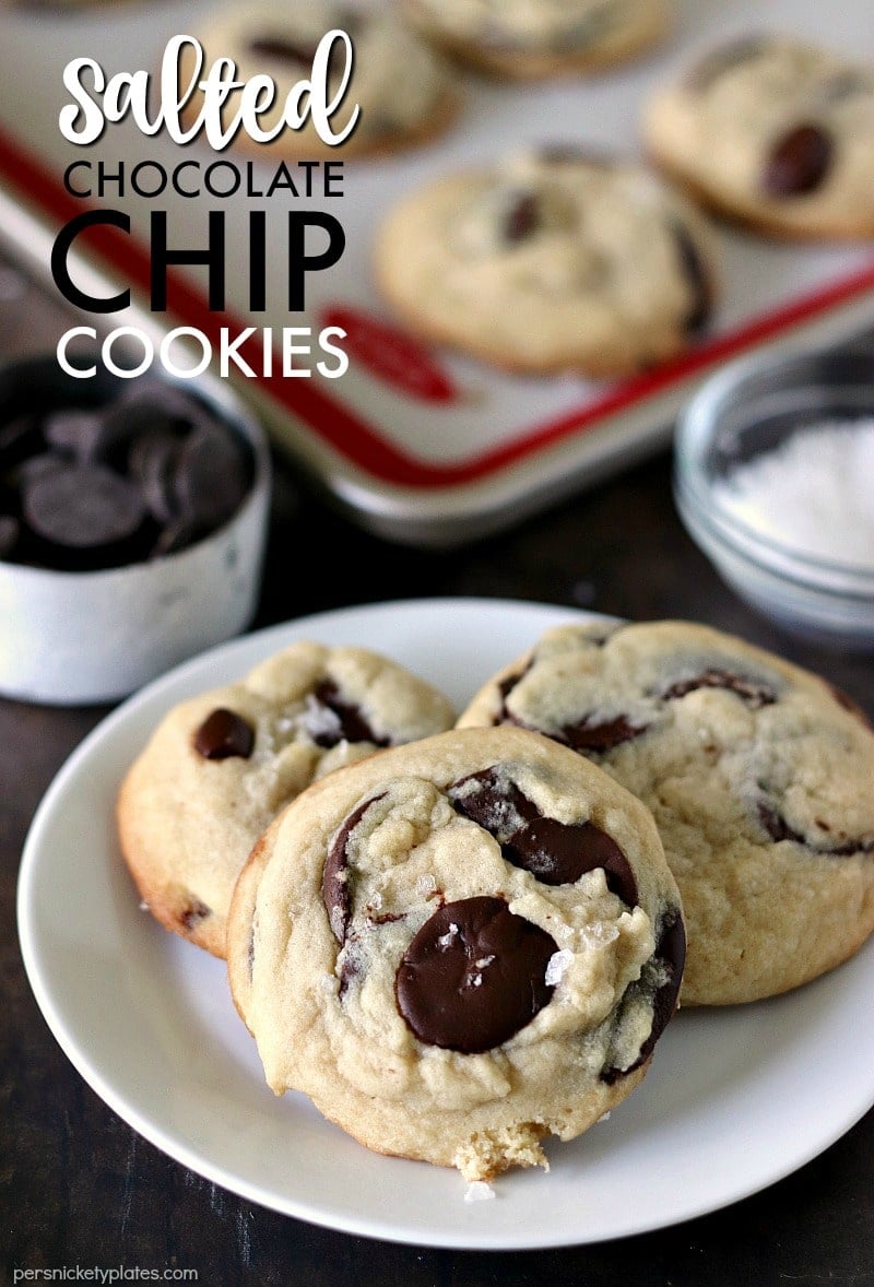 three Salted Chocolate Chip Cookies on a white plate with extras on a baking sheet