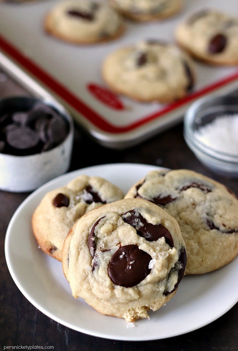 closeup of three Salted Chocolate Chip Cookies with a baking sheet of more cookies in the background