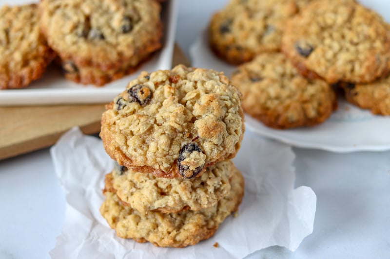 stack of 3 oatmeal raisin cookies with plates of cookies in background.