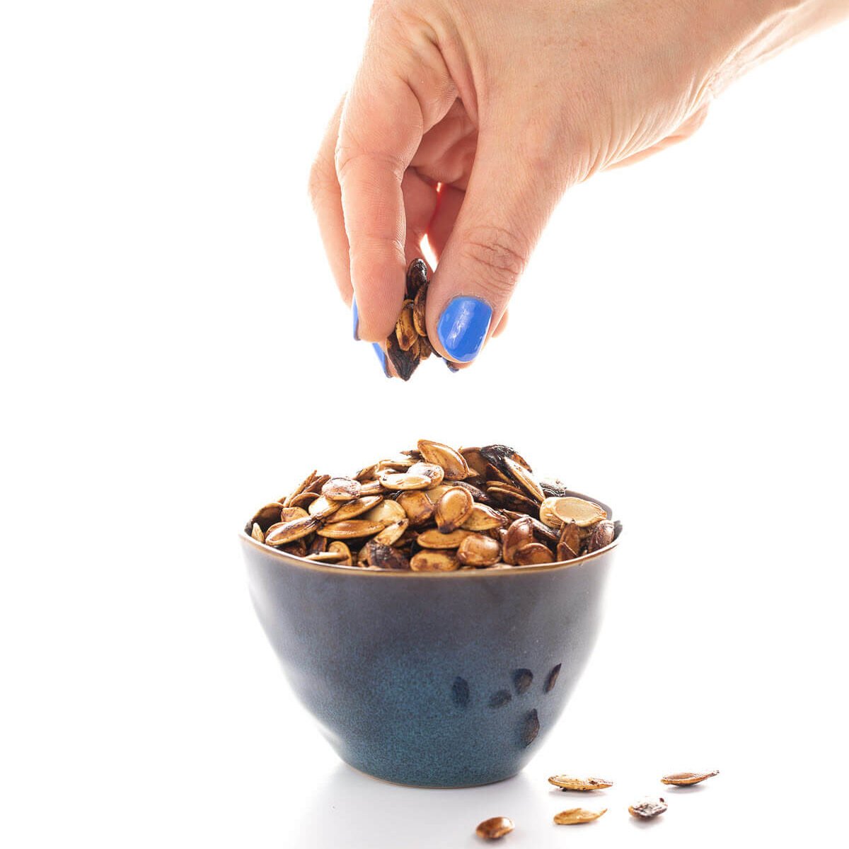 Hand grabbing roasted pumpkin seeds out of a bowl.