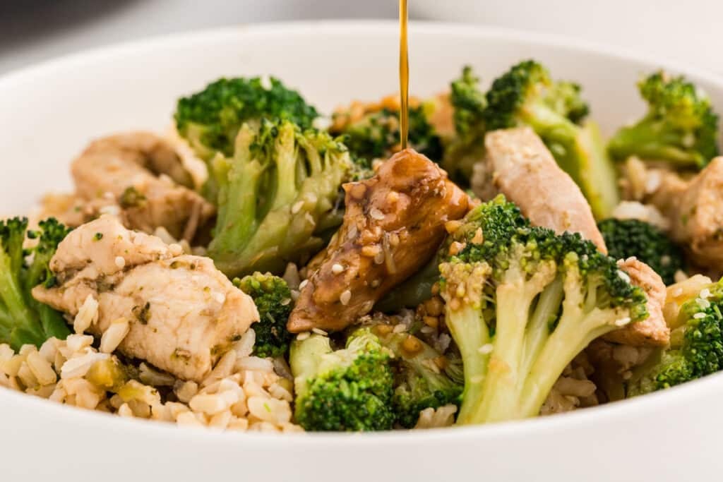 sauce drizzling over chicken and broccoli in a bowl.