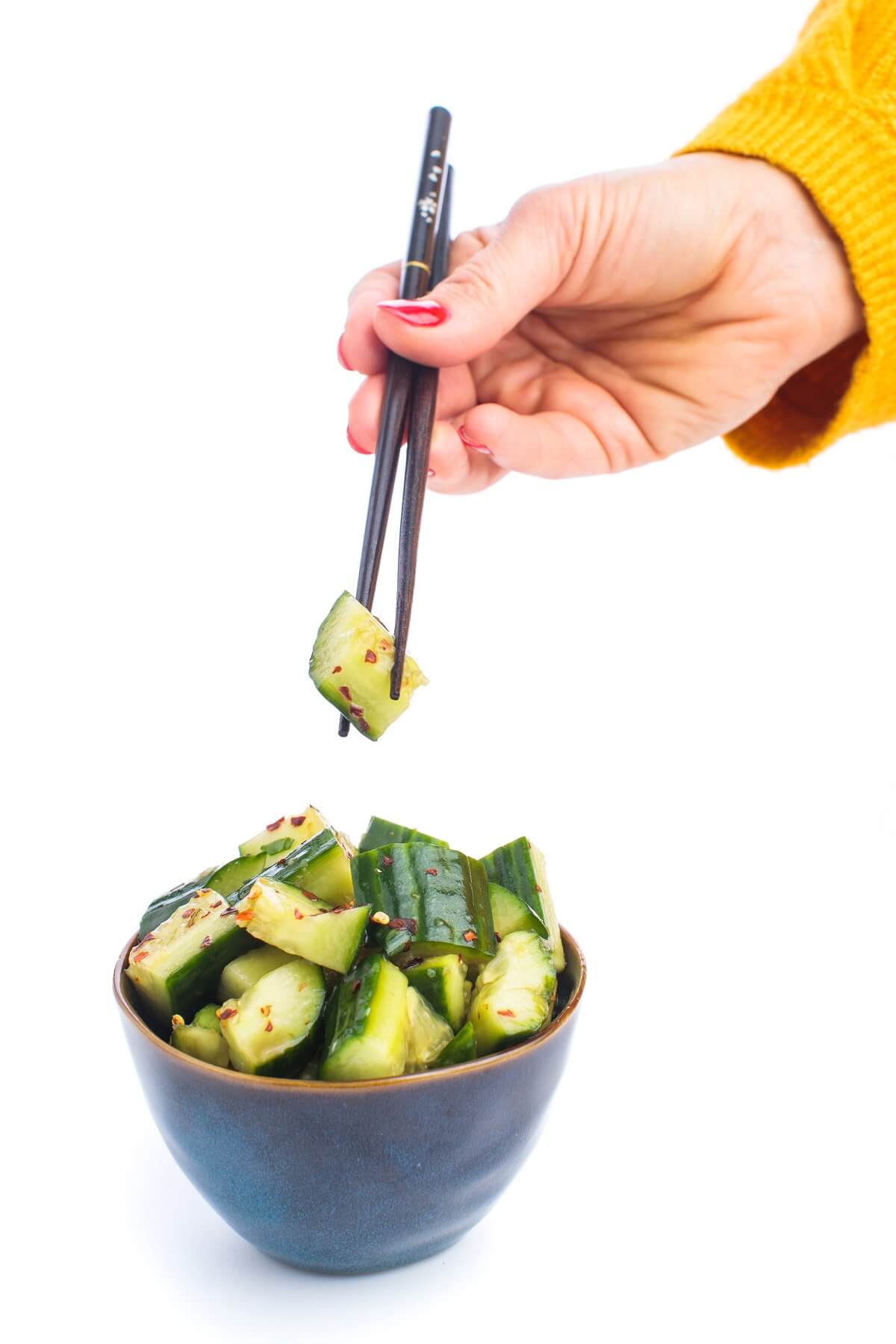 A hand using chopsticks to pick up a Chinese smashed cucumber out of a bowl.
