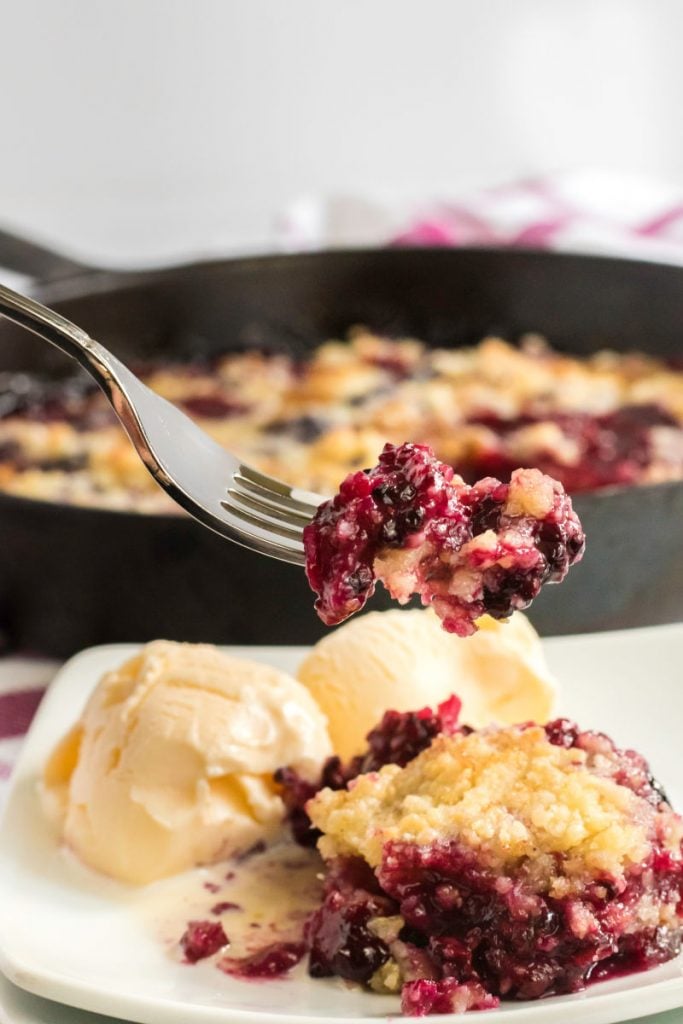 forkful of blackberry crumble served with vanilla ice cream.