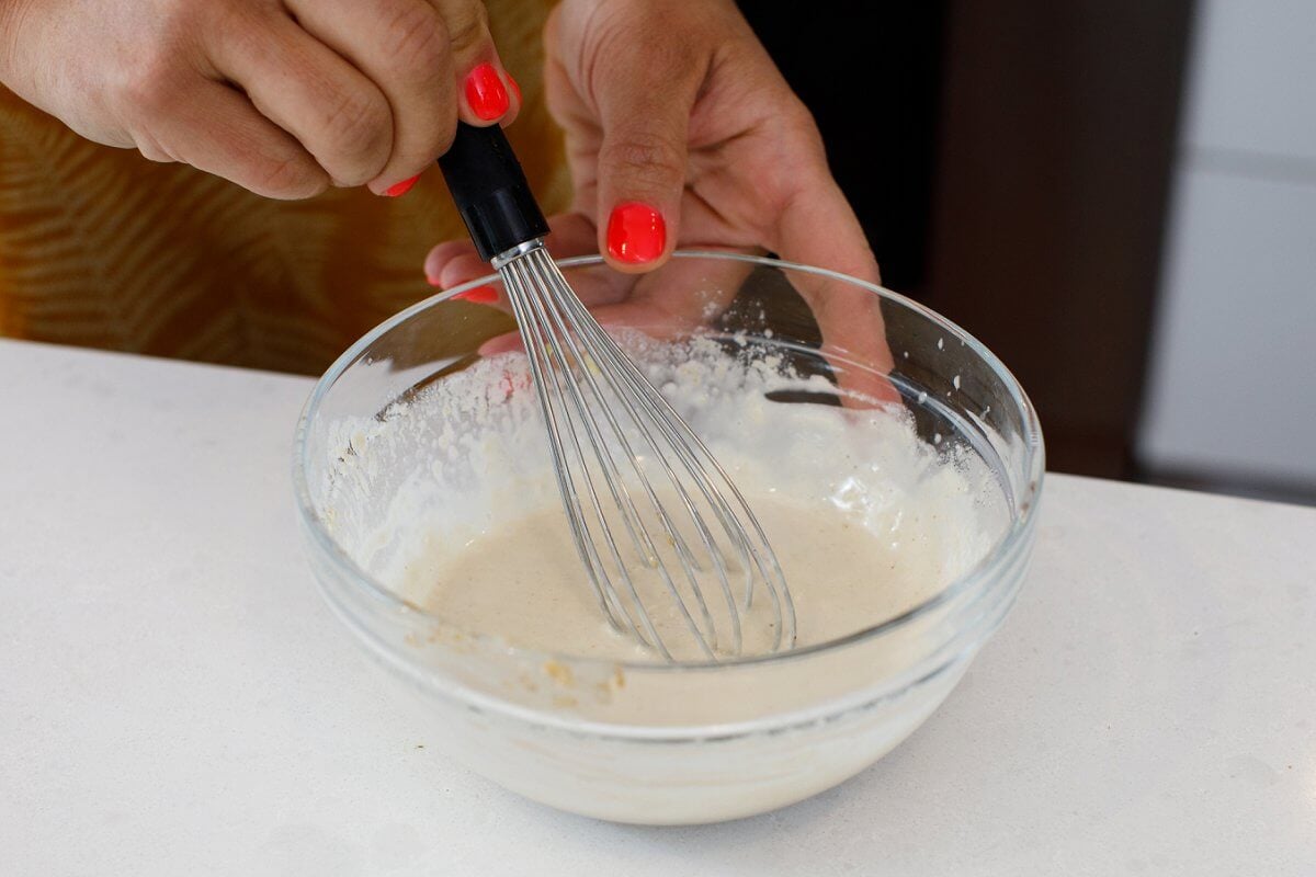 Whisking together tahini sauce in a glass bowl.