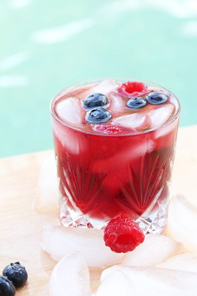 glass of berry sangria surrounded by ice cubes & fresh fruit