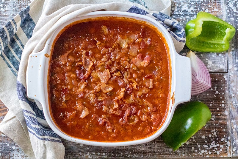overhead shot of baked beans topped with bacon in a baking dish