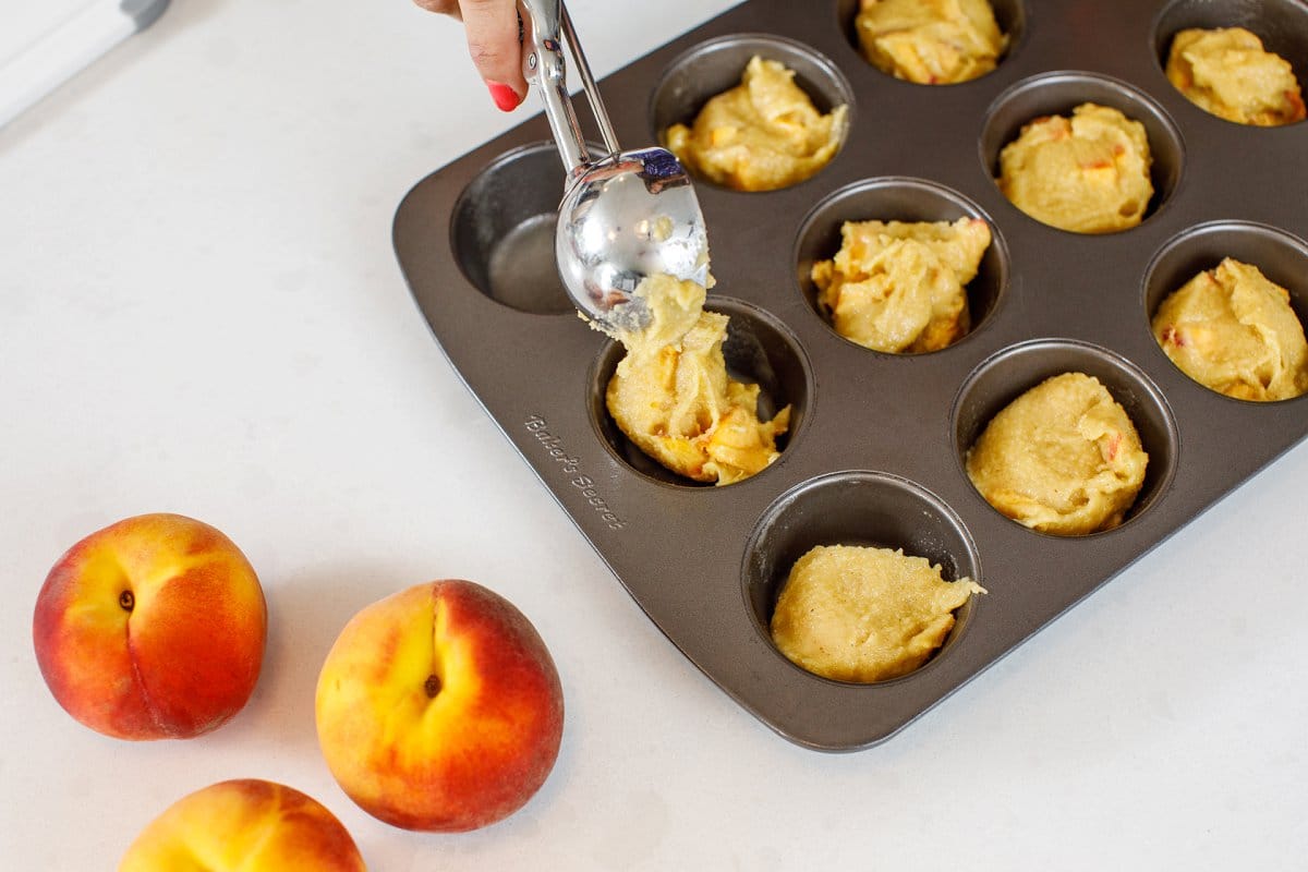 Using an ice cream scoop to portion out muffin batter into muffin tin.