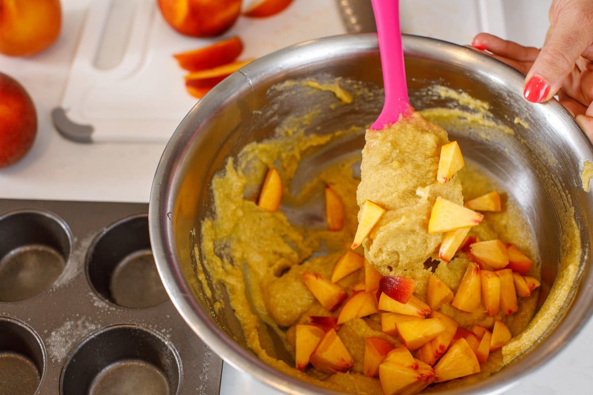 Folding in chopped peaches into muffin batter.