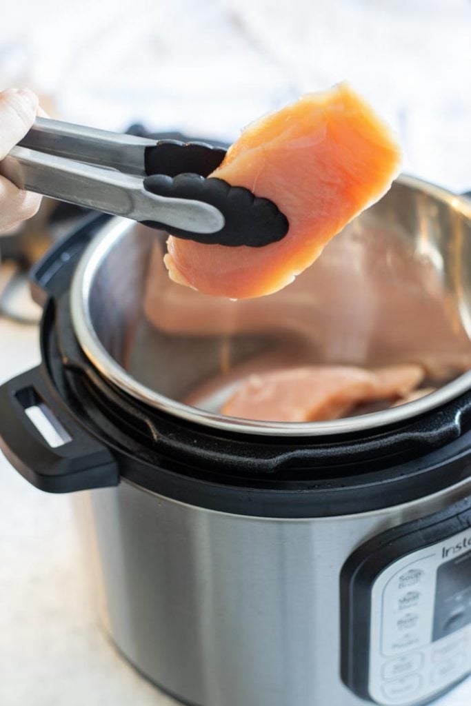 tongs placing a chicken breast into an instant pot