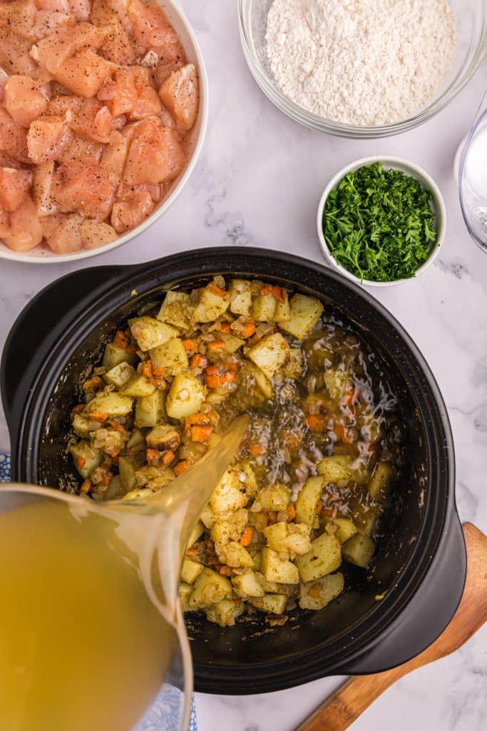 chicken stock being poured into a pot of vegetables.