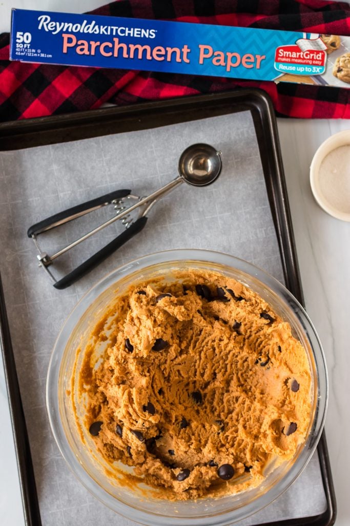 overhead shot of cookie dough bowl & cookie scoop on a baking sheet