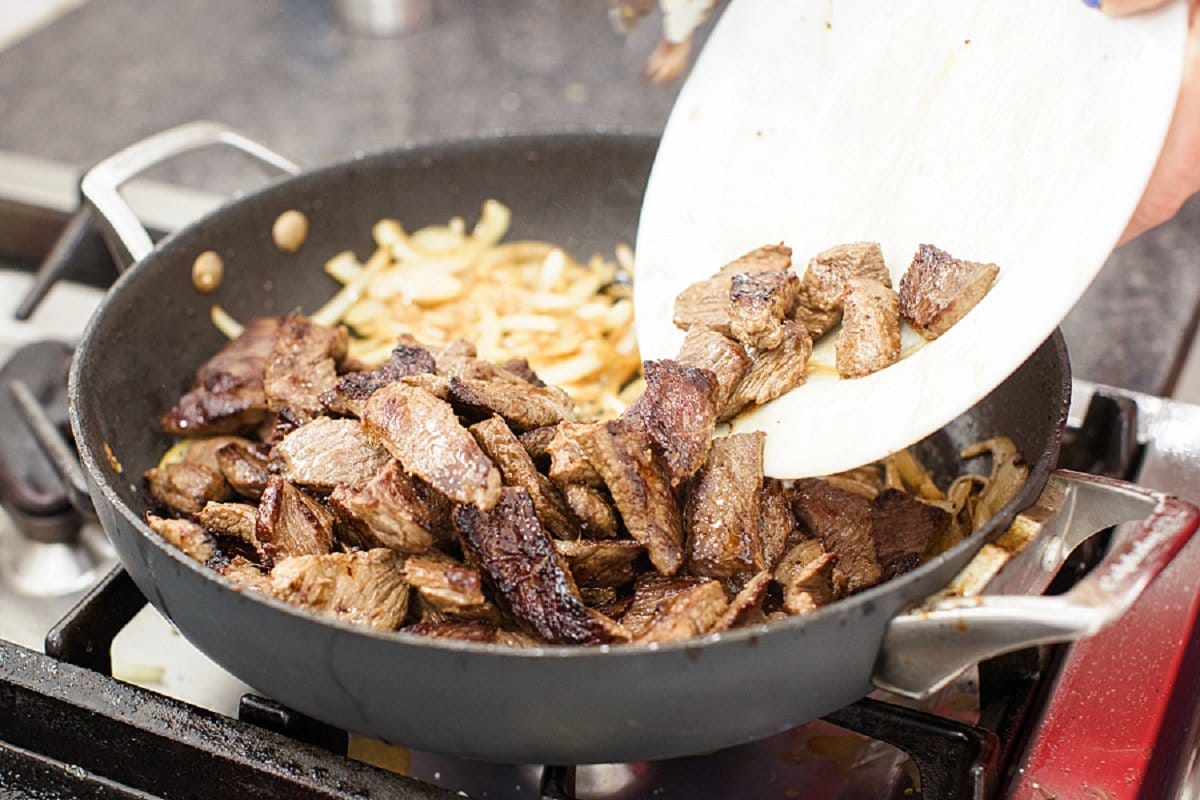 Adding cooked beef sirloin strips to pan with sautéed onions.