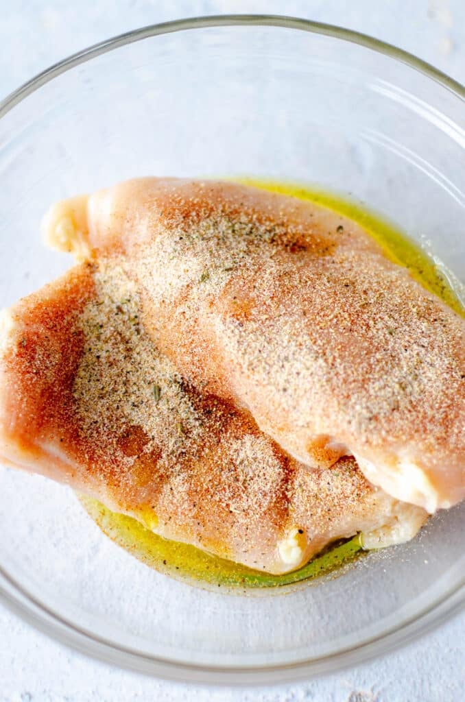 raw chicken breasts with seasoning in a bowl.