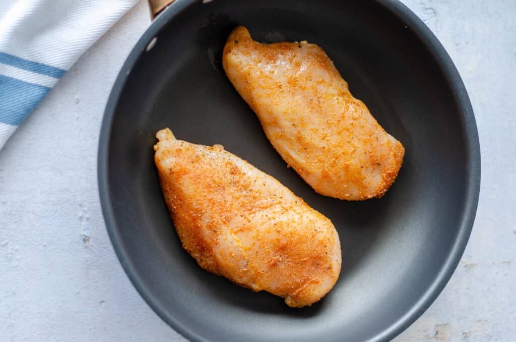 two seasoned chicken breasts in a skillet.