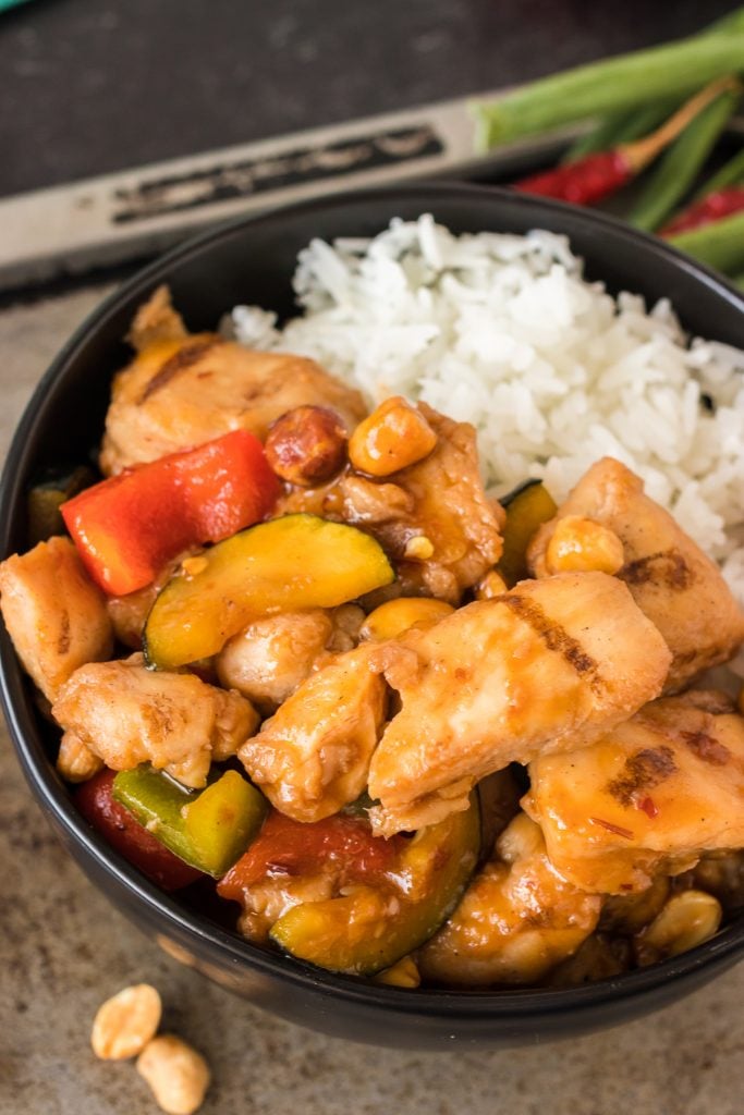 overhead shot of black bowl filled with kung pao chicken and white rice