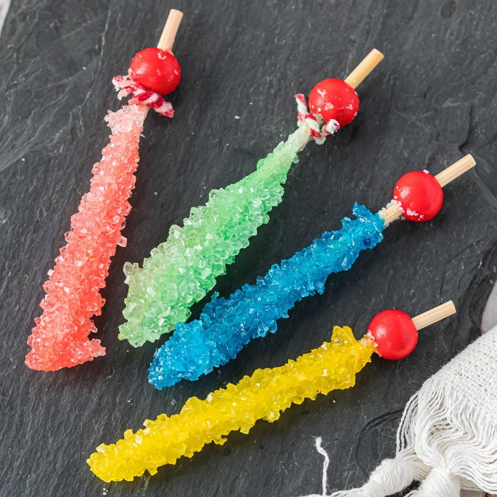 four sticks of rock candy in pink, green, blue, and yellow on a grey slab