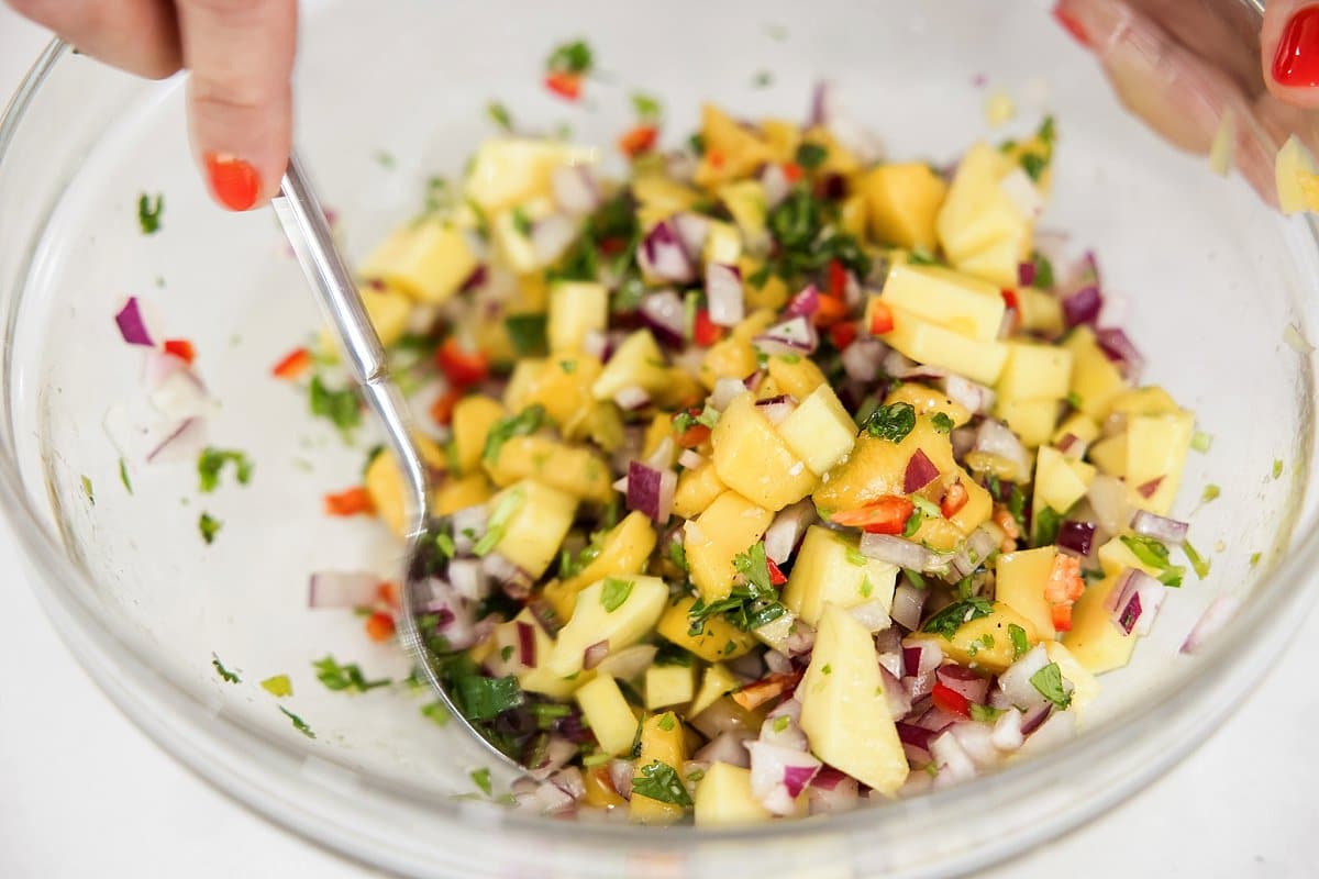 Mixing mango salsa in a large glass bowl.