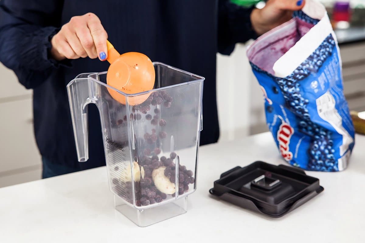 frozen blueberries being added to a blender