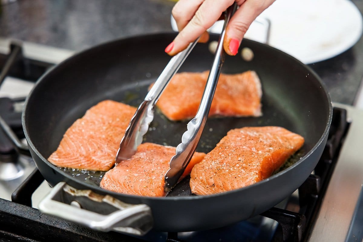 Cooking salmon fillets in a skillet on stove.
