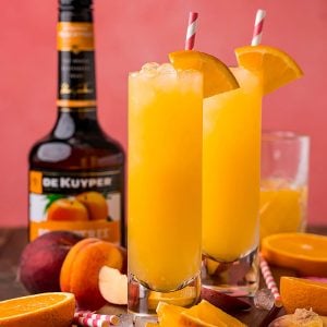 two fuzzy navel cocktails in highball glasses with orange garnish & colorful straws