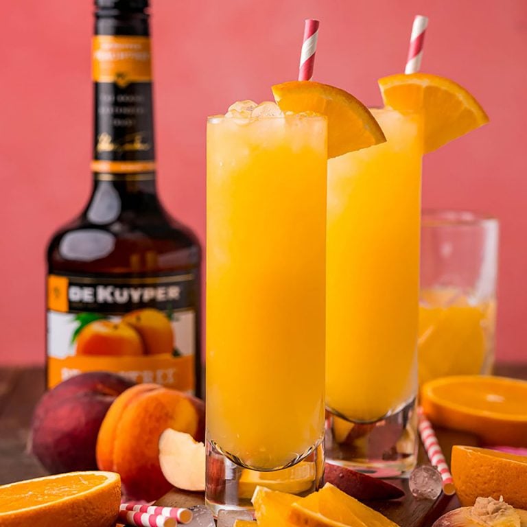 two fuzzy navel cocktails in highball glasses with orange garnish & colorful straws