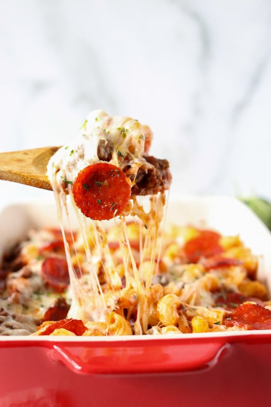 spoon pulling stretchy cheese out of a baking dish of pasta
