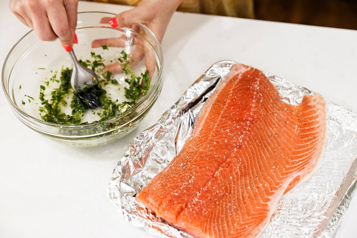 mixing herbs for baked salmon with uncooked salmon on a plate