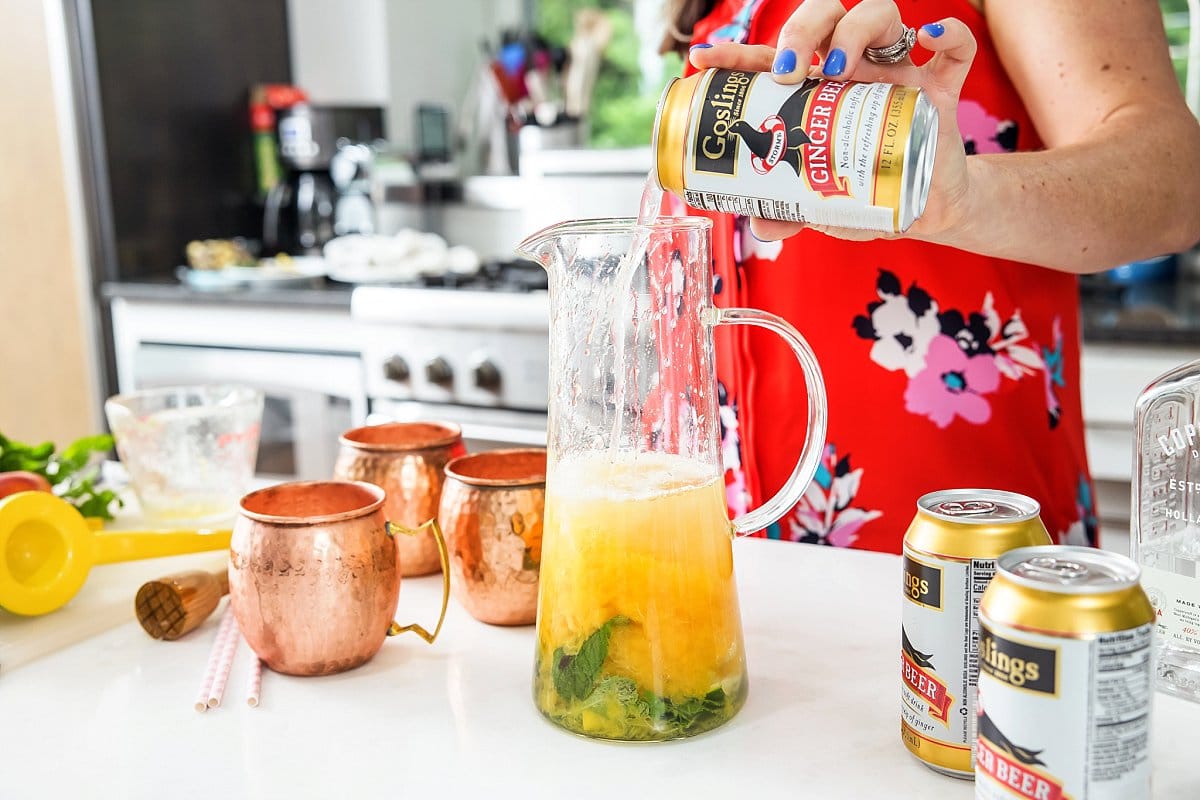 Pouring ginger beer into pitcher for peach Moscow mules.
