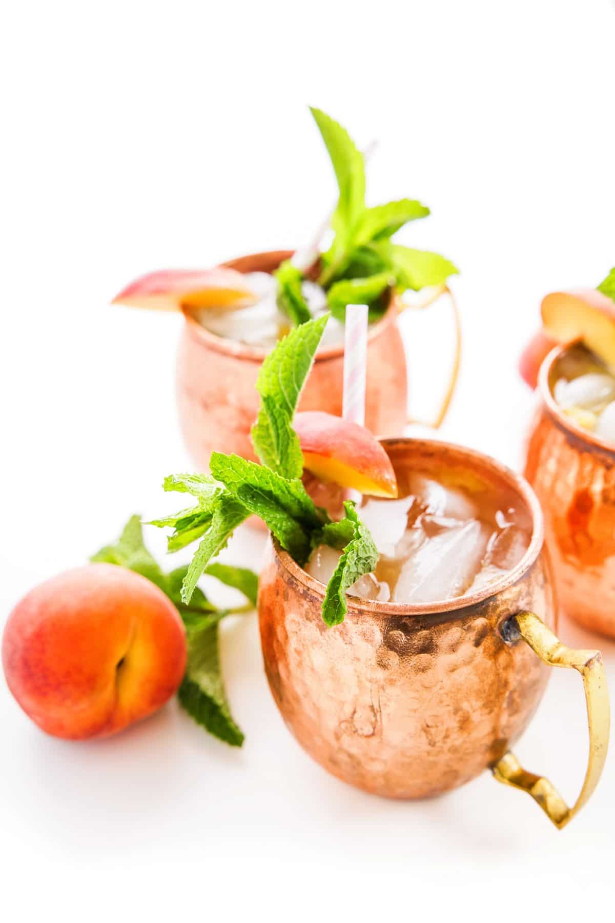 Peach Moscow mules in copper mugs, garnished with fresh mint sprigs and peach slices.