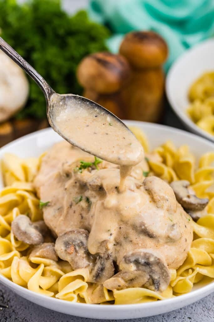 spoon drizzling gravy over chicken on egg noodles.