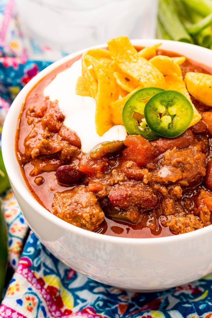white bowl of chili topped with sour cream, corn chips, and jalapenos