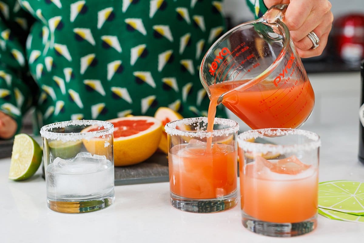 Pouring fresh grapefruit juice from a liquid measuring cup into tumblers.