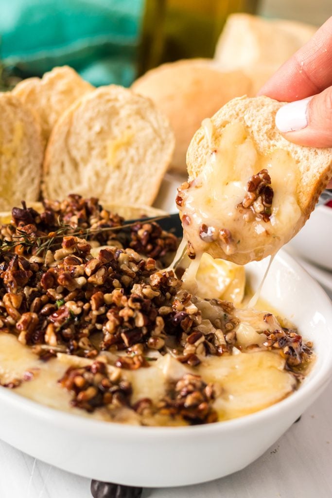 hand lifting piece of bread dipped in melty baked brie
