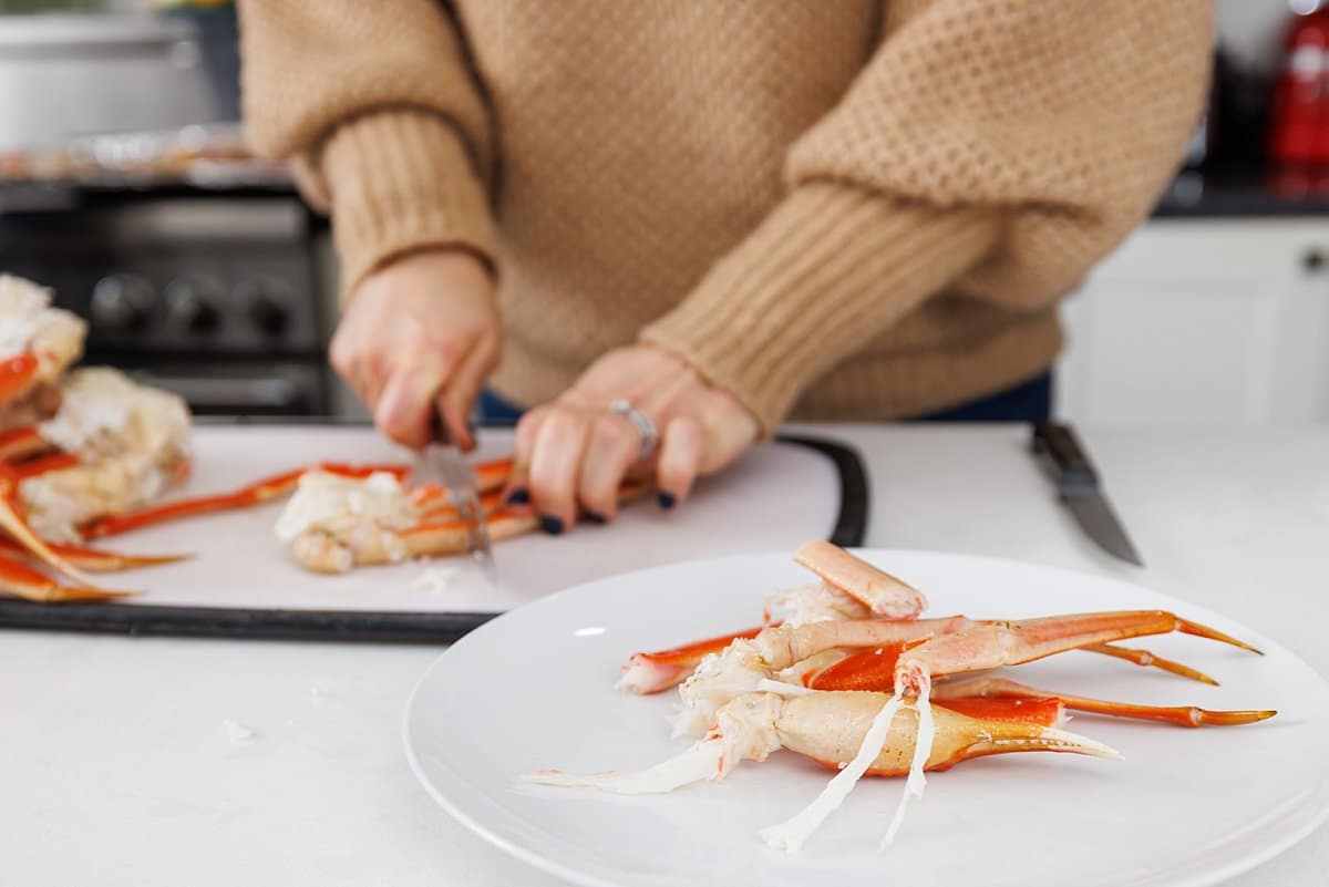 Liz trimming crab legs on a cutting board with a sharp knife.