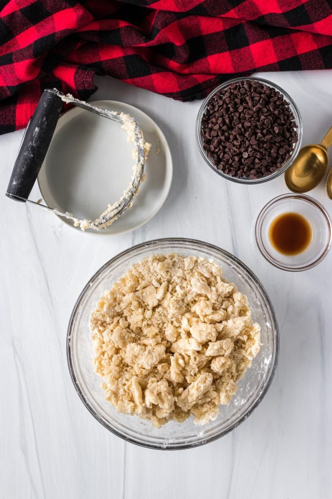 crumbly cookie dough in a mixing bowl next to a pastry cutter