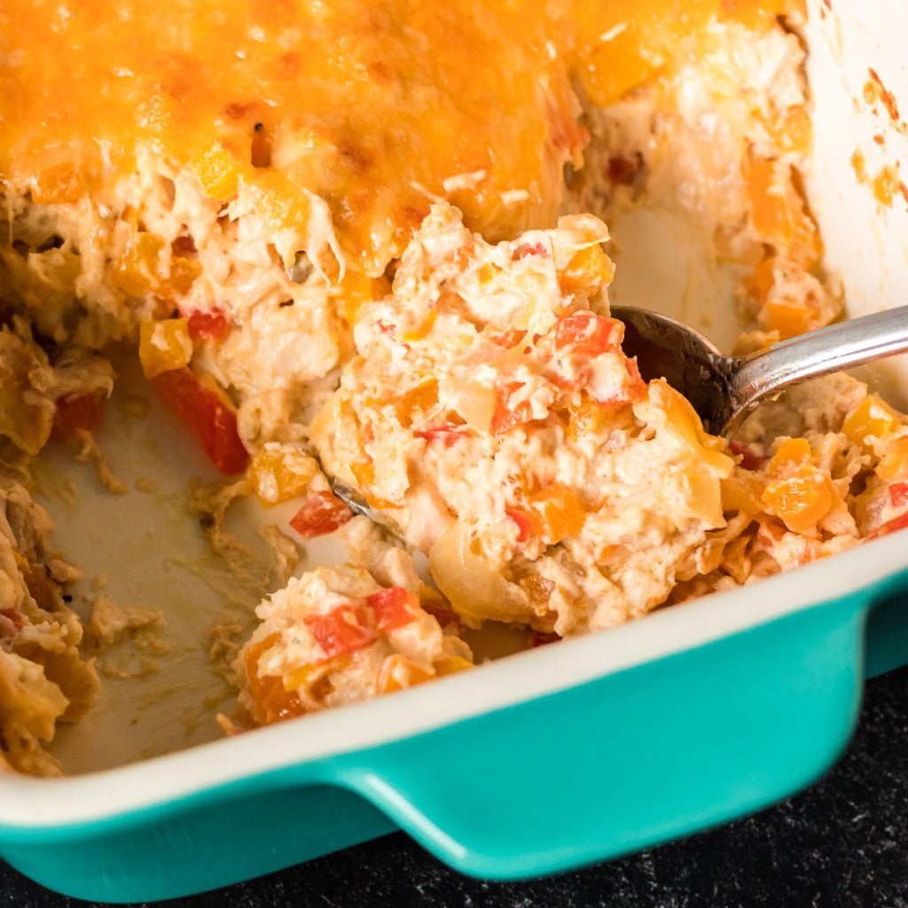 spoon scooping cheesy chicken fajita casserole from a teal baking dish