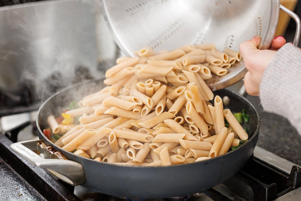 Adding cooked penne pasta to pan with chard and chicken.