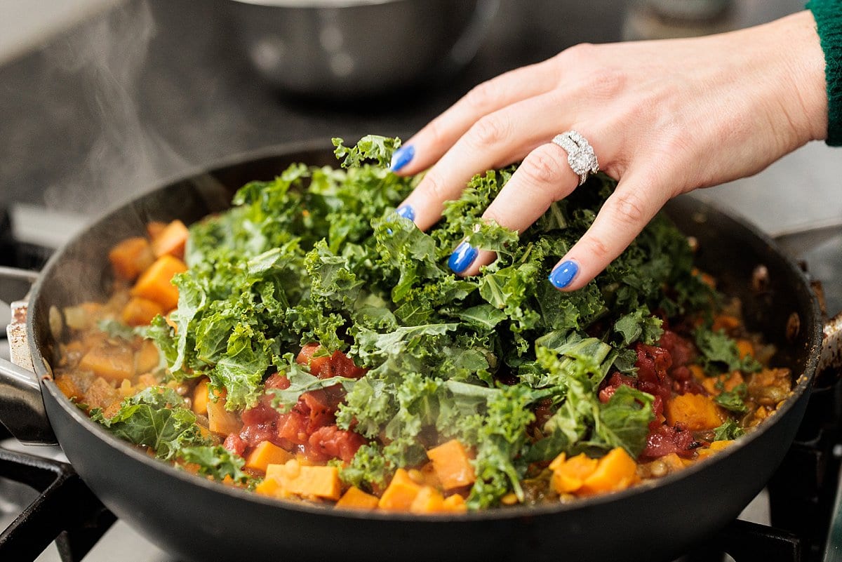 Adding kale to skillet with sweet potatoes and roasted tomatoes.