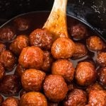 wooden spoon scooping grape jelly meatballs from a crockpot.