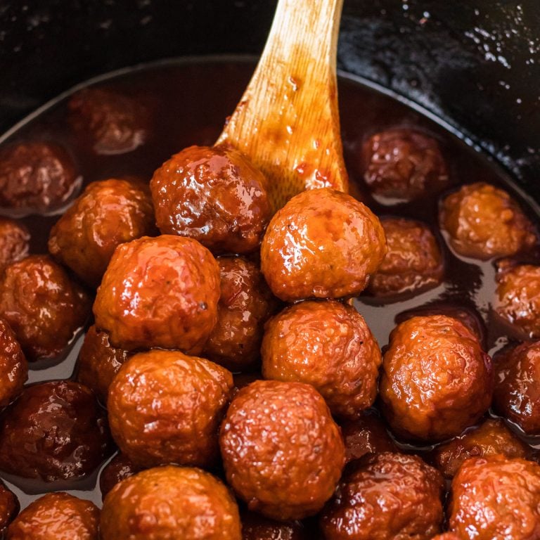 wooden spoon scooping grape jelly meatballs from a crockpot.