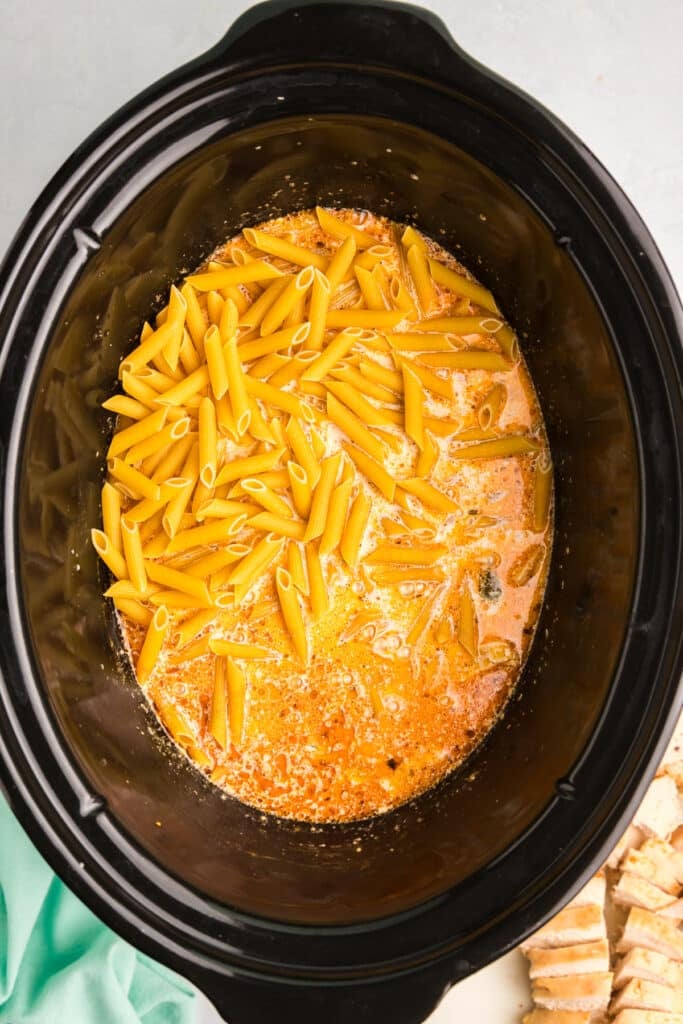 penne pasta poured into a black crockpot.