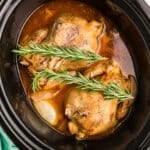 Two cooked Cornish hens in a crockpot with sprigs of rosemary.