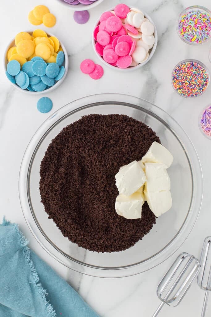 overhead shot of Oreo crumbs and cream cheese cubes in a mixing bowl.